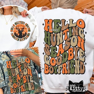 Puede incluir: Sudadera blanca con el texto "HELLO HUNTING SEASON GOODBYE BOYFRIEND" en naranja, verde y marrón. Una segunda sudadera de camuflaje tiene el mismo texto. También se ve un gráfico circular con un ciervo y el mismo texto.