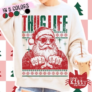 May include: Cream-colored sweatshirt with a red and green graphic of Santa Claus wearing sunglasses and the words "THUG LIFE". The design includes a Christmas sweater pattern and the text "HO-HO".