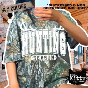 May include: Camouflage-patterned t-shirt with the words "HUNTING SEASON" in white block letters. The shirt has a distressed look and is available in two colors. The image also includes the text "DISTRESSED & NON DISTRESSED INCLUDED".