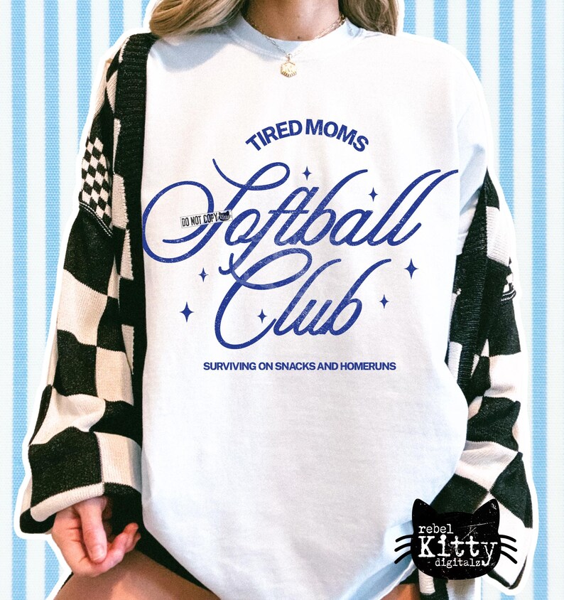 May include: White sweatshirt with the text "TIRED MOMS Softball Club" in blue script. The sweatshirt also has the phrase "SURVIVING ON SNACKS AND HOMERUNS" below the club name. The sleeves are partially covered by a black and white checkered cardigan.