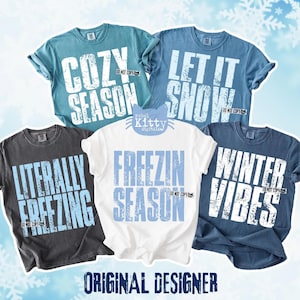 May include: Five t-shirts with winter-themed phrases in white lettering. The shirts are various colors, including teal, blue, white, and charcoal. Phrases include "Cozy Season," "Let It Snow," "Literally Freezing," "Freezin Season," and "Winter Vibes."