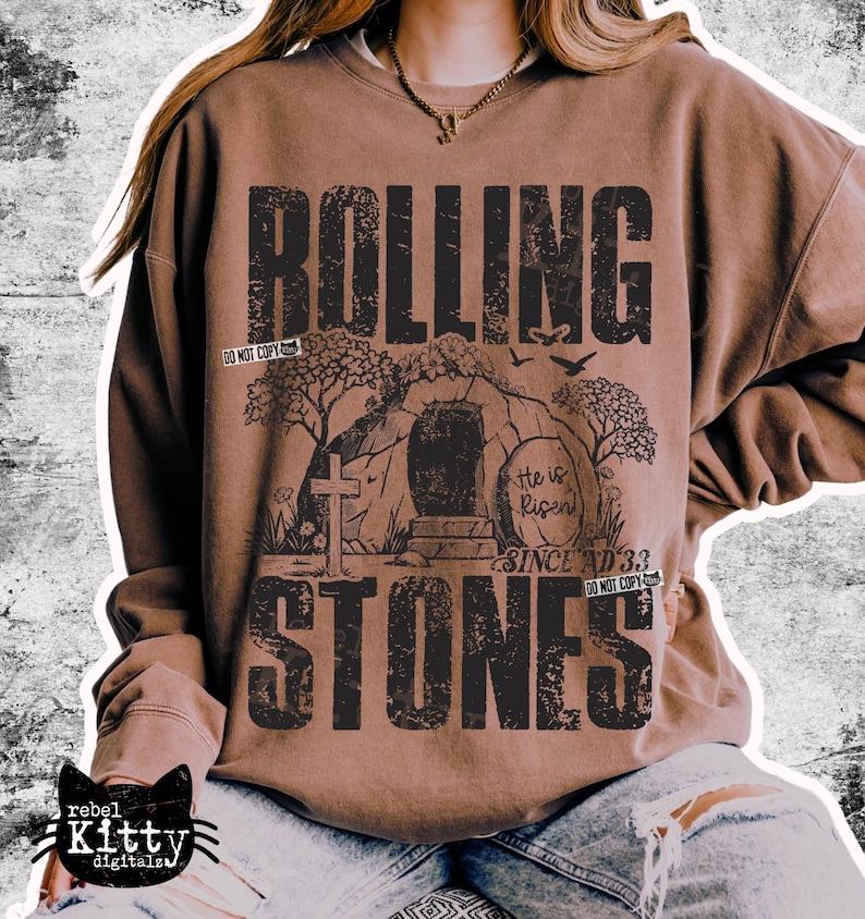 May include: Brown sweatshirt with a distressed graphic that reads "Rolling Stones" in large, black letters. The graphic includes an illustration of a tomb, cross, and the text "He is Risen Since AD 33".