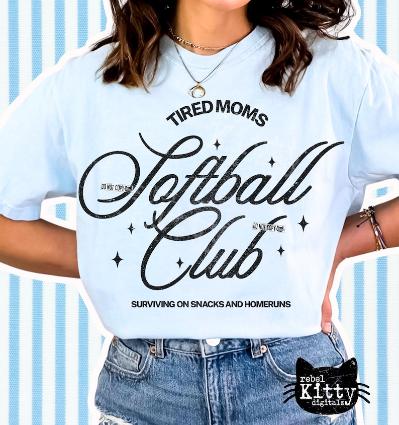 May include: Light blue t-shirt with the text "TIRED MOMS Softball Club" in black script. The shirt also features the phrase "SURVIVING ON SNACKS AND HOMERUNS". The shirt is worn with blue denim shorts.