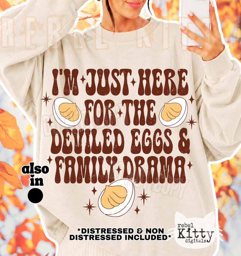 May include: A beige crewneck sweatshirt featuring brown text that reads I'M JUST HERE FOR THE DEVILED EGGS & FAMILY DRAMA. The design includes illustrations of three halved deviled eggs and small four-pointed stars. The text has a distressed texture.