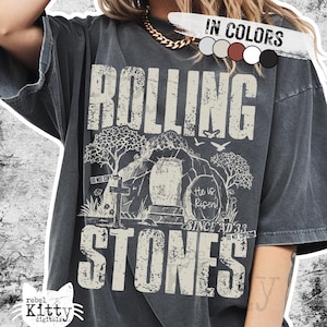 Pode incluir: T-shirt cinzenta escura com as palavras "ROLLING STONES" em uma fonte desgastada. O gráfico inclui uma cena de túmulo com o texto "He is Risen! Since AD 33". A camisa também tem o texto "DO NOT COPY".