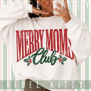 May include: A white long-sleeve sweatshirt featuring the red distressed text MERRY MOM and the green cursive text Club. The design includes two green holly leaf sprigs with red berries positioned on either side of the word Club on the front.