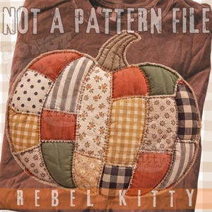 May include: A brown t-shirt featuring a large, central pumpkin graphic composed of various fabric patches in shades of orange, green, brown, and cream. The pumpkin design includes polka dot, striped, floral, and gingham patterns with visible stitching.