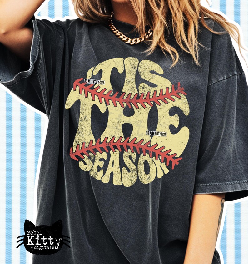 May include: Black t-shirt with a distressed graphic. The graphic features the words "TIS THE SEASON" in a vintage style, with a baseball design. The shirt has a relaxed fit and short sleeves. The Rebel Kitty Digitals logo is in the bottom left corner.