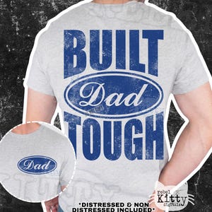 May include: Light grey t-shirt with a blue distressed design that reads "BUILT Dad TOUGH". The word "Dad" is inside an oval. The shirt has a crew neck and short sleeves.