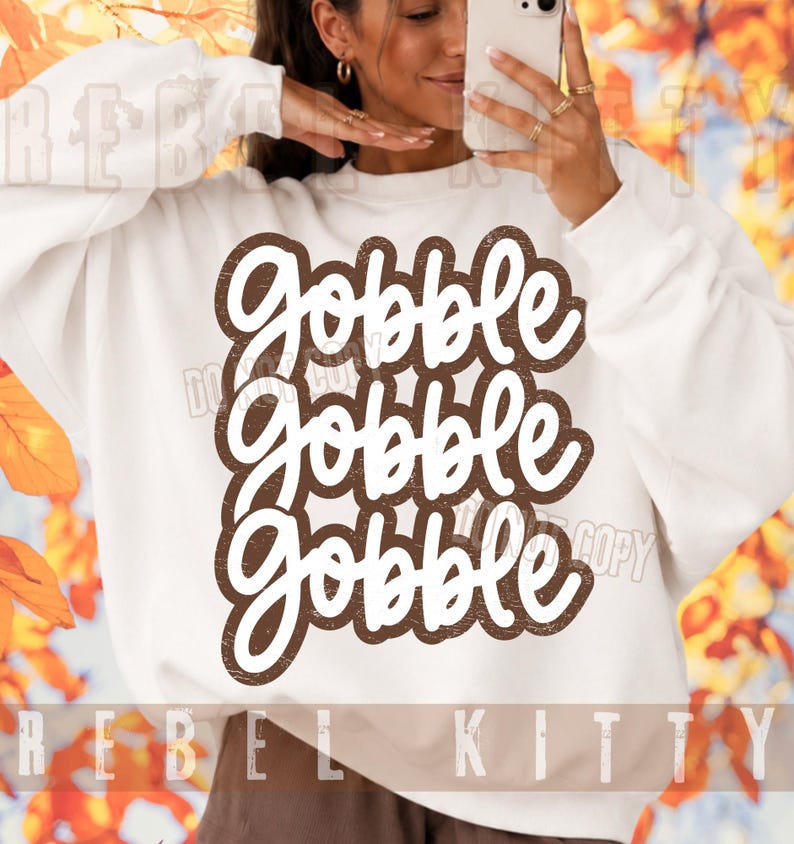 May include: A white long-sleeve sweatshirt featuring the text Gobble Gobble Gobble in a stacked, brown, distressed-style font. The lettering is bold and rounded, centered on the chest of the garment, creating a clear and legible graphic design.