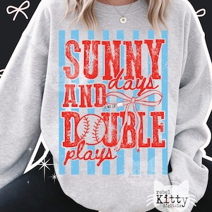 May include: A light grey sweatshirt with a baseball design. The design features the words "SUNNY AND days DOUBLE plays" in red, with a baseball graphic and light blue vertical stripes. The text "DO NOT COPY" is also visible.