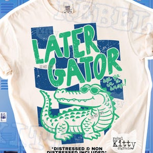 Peut inclure: T-shirt crème avec un motif vert et bleu vieilli. Le motif présente les mots "LATER GATOR" au-dessus d'un alligator de dessin animé portant des lunettes de soleil. La phrase "See ya in a snap!" est également incluse.