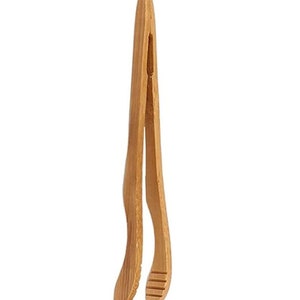 Puede incluir: Un par de pinzas de madera natural con un diseño curvo. Las pinzas están hechas de bambú y tienen un acabado liso y pulido.