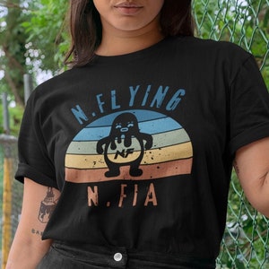 May include: Black t-shirt featuring a retro-style graphic of a penguin with the text "N.Flying N.Fia".