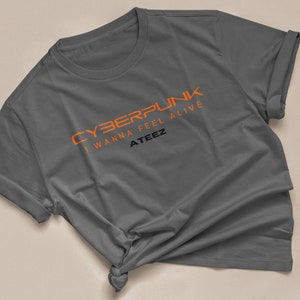 Może przedstawiać: Szary t-shirt z napisem "CYBERPUNK I WANNA FEEL ALIVE ATEEZ" w kolorze pomarańczowym.