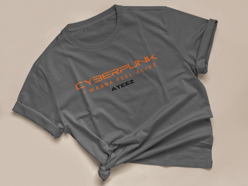 Może przedstawiać: Szary t-shirt z napisem "CYBERPUNK I WANNA FEEL ALIVE ATEEZ" w kolorze pomarańczowym.