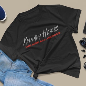 K&ouml;nnte beinhalten: Schwarzes T-Shirt mit dem Text "XPINARY HEROES WE ARE ALL HEROES" in wei&szlig;er und roter Schrift.