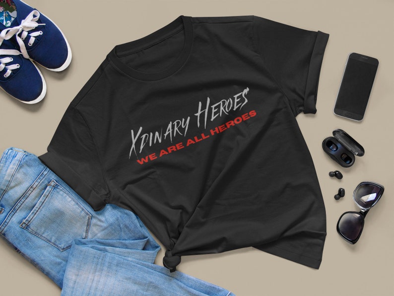 K&ouml;nnte beinhalten: Schwarzes T-Shirt mit dem Text "XPINARY HEROES WE ARE ALL HEROES" in wei&szlig;er und roter Schrift.