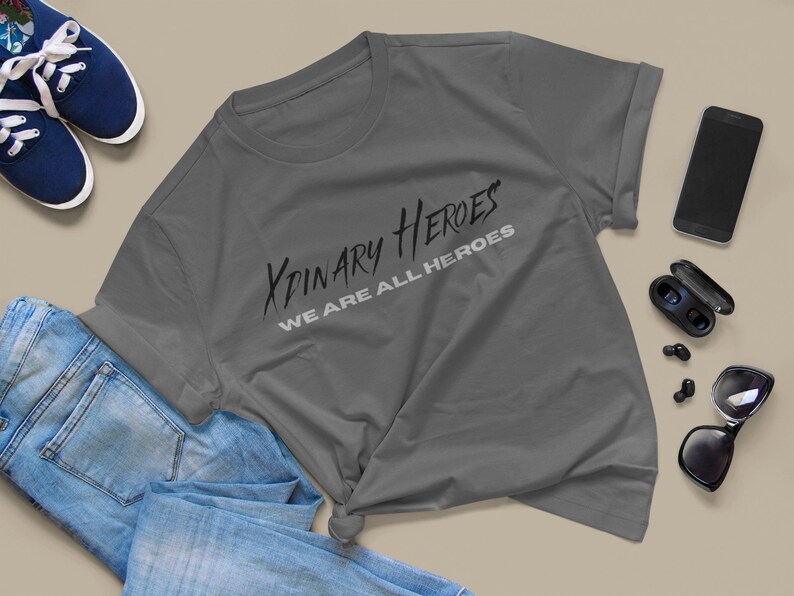 K&ouml;nnte beinhalten: Ein anthrazitfarbenes T-Shirt mit dem Aufdruck "XPINARY HEROES WE ARE ALL HEROES" in Schwarz und Wei&szlig;.