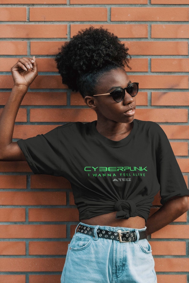 Może przedstawiać: Czarny T-shirt z zielonym tekstem, kt&oacute;ry brzmi "CYBERPUNK I WANNA FEEL ALIVE ATEEZ". Osoba w tym T-shircie stoi przed ceglaną ścianą.
