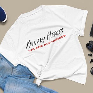 K&ouml;nnte beinhalten: Wei&szlig;es T-Shirt mit schwarzem und rotem Text, der "XPINARY HEROES WE ARE ALL HEROES" lautet.