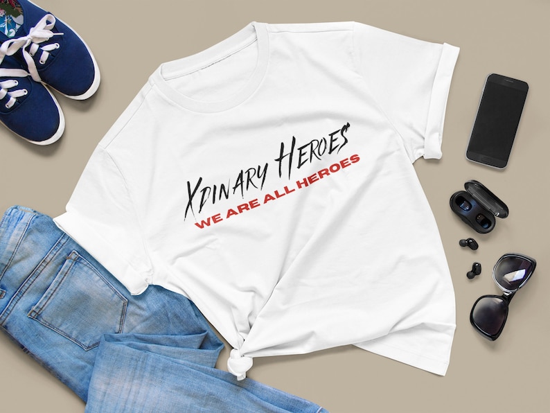K&ouml;nnte beinhalten: Wei&szlig;es T-Shirt mit schwarzem und rotem Text, der "XPINARY HEROES WE ARE ALL HEROES" lautet.