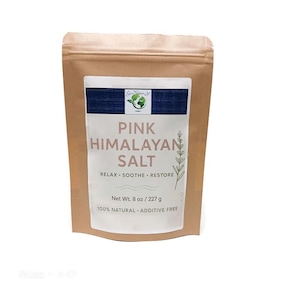 Puede incluir: Una bolsa de papel marrón con sal rosa del Himalaya. La etiqueta presenta el texto "Pink Himalayan Salt" con las palabras "Relax, Soothe, Restore" debajo. El peso neto es de 227 g. La etiqueta también indica "100% Natural, Additive Free".