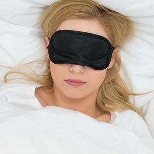 Black Sleep Mask covering the eyes of a woman lying in bed.