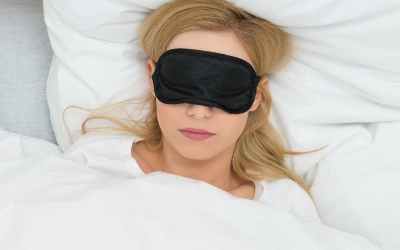Black Sleep Mask covering the eyes of a woman lying in bed.