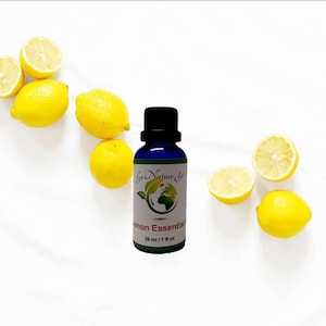 Puede incluir: Una botella de vidrio azul con una etiqueta blanca que dice "Go Nature" y "Lemon Essential Oil 29 ml / 1 fl oz". La botella está rodeada de limones sobre un fondo blanco.