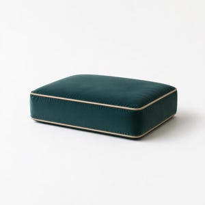 May include: A rectangular floor cushion upholstered in deep teal velvet fabric. The cushion features a smooth, soft-touch surface and is finished with a light beige piping trim that outlines the top and bottom edges of the rectangular form.