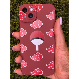 May include: A maroon phone case featuring a pattern of red and white cloud designs and a central emblem. The case has a camera cutout and is held in a hand with painted nails. The case is designed for a smartphone.