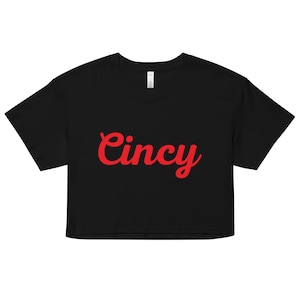 Puede incluir: Camiseta negra recortada con la palabra "Cincy" en letras rojas cursivas.
