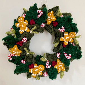 Puede incluir: Una corona de Navidad de punto verde decorada con hombres de jengibre, bastones de caramelo y hojas de acebo.