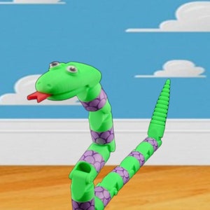 May include: A green and purple segmented snake toy with a red tongue. The snake is posed in a 'S' shape with its head facing the viewer.