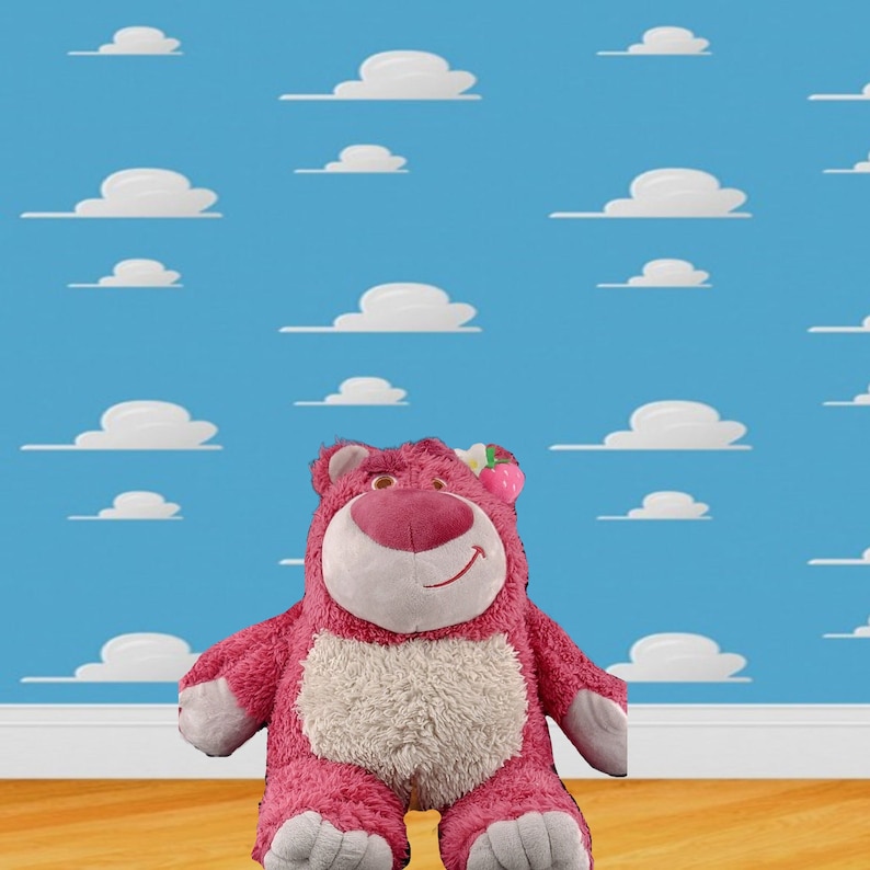 May include: Pink plush toy bear with a white belly and a pink flower on its head. The bear is sitting on a wooden floor in front of a blue wall with white clouds.