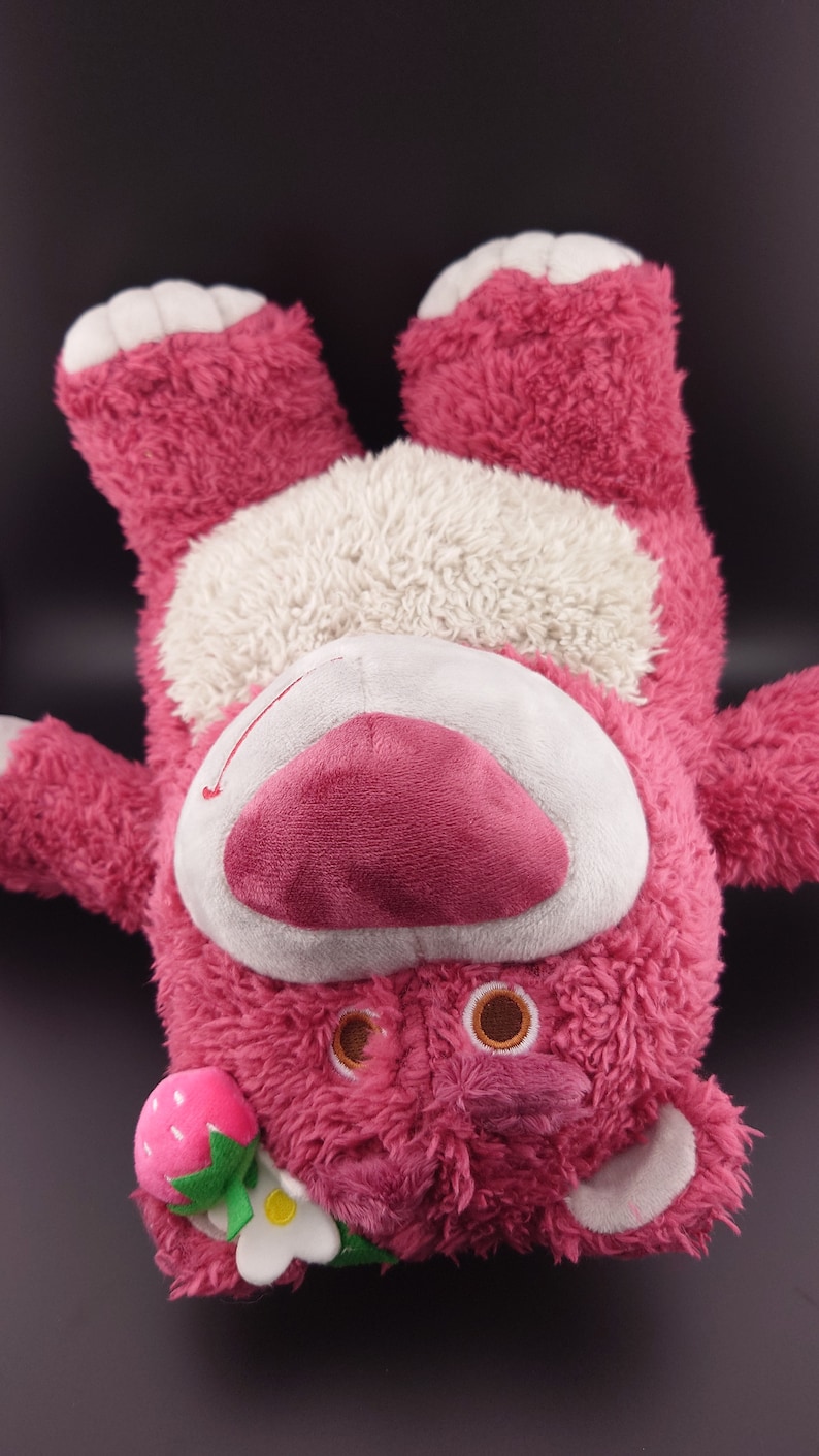 May include: Pink plush toy bear with a white belly and a strawberry and flower on its head.