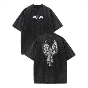May include: A charcoal grey acid-wash t-shirt featuring a white graphic print. The front displays a small sword with wings, while the back features a large, detailed illustration of a sword centred between two expansive, feathered angel wings.