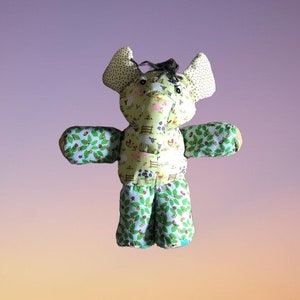 May include: A green and yellow stuffed elephant toy with a farm animal print. The elephant has large ears and a long trunk.