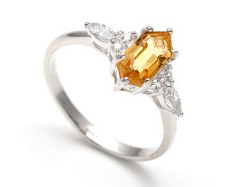 May include: A silver ring featuring a large, rectangular, yellow gemstone as the focal point. The ring is accented with smaller, clear gemstones and has a delicate band. The ring is set against a white background.