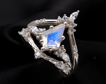May include: A silver ring with a large, iridescent moonstone set in a geometric shape. The ring is accented with smaller, clear stones.