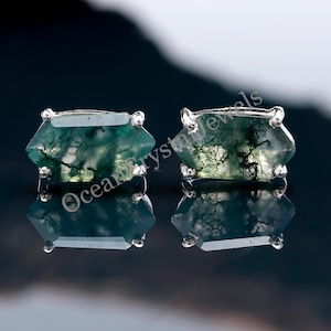 May include: A pair of silver earrings with green moss agate stones. The stones are cut in a hexagonal shape and have a natural, organic look.