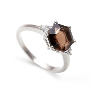 May include: A silver ring featuring a brown hexagonal gemstone surrounded by smaller clear gemstones.