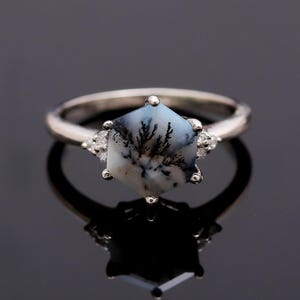 May include: A silver ring with a hexagonal dendritic agate gemstone and three small diamonds. The ring is set on a black background.