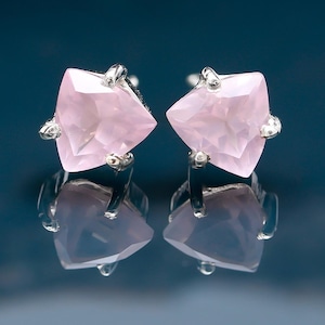 Op de afbeelding: Een paar zilveren oorbellen met roze edelsteen accenten. De edelstenen zijn driehoekig van vorm en hebben een facetgeslepen.