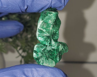 May include: A green malachite crystal with a unique, organic shape. The crystal has a smooth, polished surface and a deep green color.