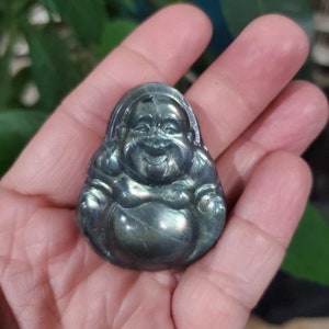 May include: A small, smiling Buddha figurine carved from a dark, iridescent stone. The Buddha is depicted in a seated position with a rounded belly and a serene expression. The stone has a mix of green and blue hues.