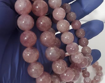 Può includere: Tre braccialetti di pietre preziose rosa con perline rotonde. I braccialetti sono impilati uno sopra l'altro e sono tenuti in una mano guantata.