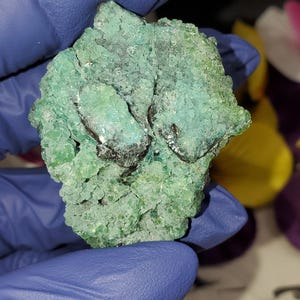 May include: A green and blue crystal cluster with a rough, textured surface. The crystal is a natural formation with a unique shape.