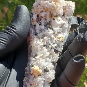May include: A cluster of white, gray, and brown crystals with a rough, natural texture. The crystals are arranged in a dense, irregular formation.